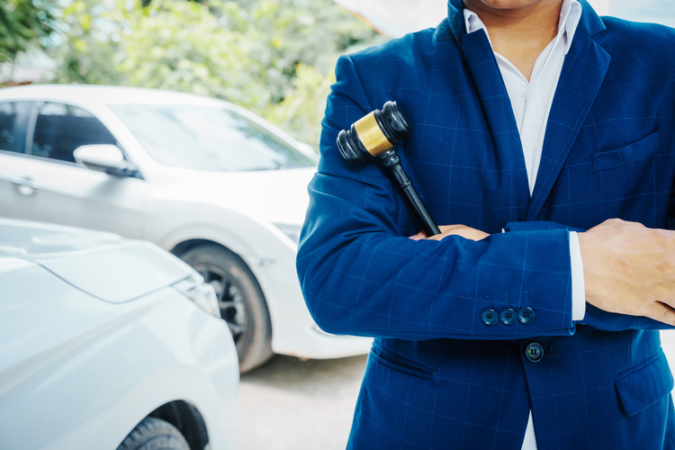 Businessman in a suit and a lawyer, holding a wooden gavel, stand in front of a car.